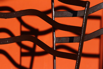 Detail of iron chairs in the sun. Crossing of lines. Orange colored wall background.
