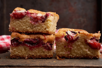 stack of square baked sponge cake slices with plums on wooden kitchen board
