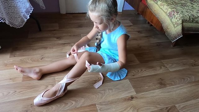 Young little ballerina taking on pointe shoes at home. Dreams and ballet dance concept