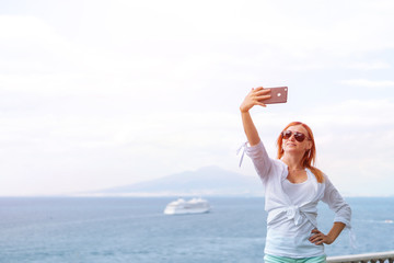 Pretty girl Takes a selfie photo. Sea and horizon in the background. Vacation and travel concept. Communication on a mobile network. Internet, stay right. Vesuvius volcano and ocean liner. Copy space