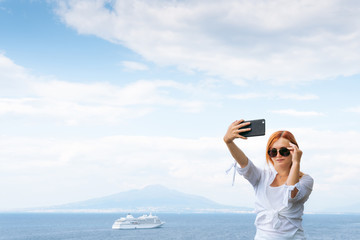 Pretty girl in sunglasses Takes a selfie photo. Sea and horizon in the background. Vacation and travel concept. Communication on a mobile network. Internet Vesuvius volcano and ocean liner. Copy space