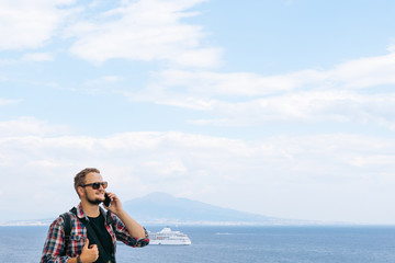 Male tourist takes the call. Shares impressions and information, uses a smartphone. Communication and mobile internet concept. Roaming. View of the sea and Mount Vesuvius. Ocean liner. Copy space