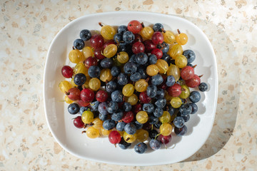 white plate with berries on the table. Blueberries, colored gooseberries