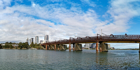 Beautiful panoramic view of a railway bridge across a river on a sunny day with deep blue sky and light clouds, Parramatta river, Meadowbank, Sydney, New South Wales, Australia
