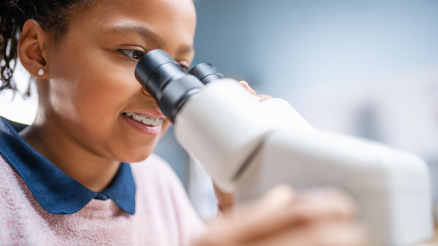 Portrait of Smart Little Schoolgirl Looking Under the Microscope. In Elementary School Classroom Cute Girl Uses Microscope. STEM (science, technology, engineering and mathematics) Education Program
