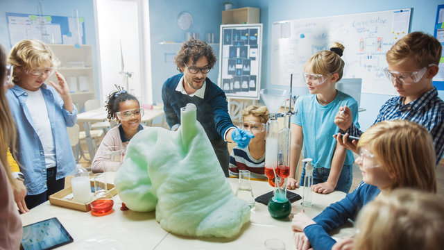 Elementary School Science / Chemistry Classroom: Enthusiastic Teacher Shows Funny Chemical Reaction Experiment to Group of Children. Mixing Chemicals in Beaker so they Shoot Foam (Elephant Toothpaste)