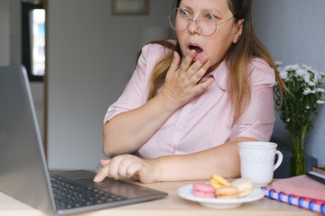 very surprised middle-aged woman sitting at her desk on the Internet, a plate of macaroon cakes, technology concept, unexpected information on the Internet, shock content