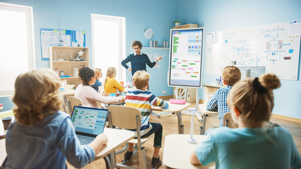 Elementary School Computer Science Teacher Uses Interactive Digital Whiteboard to Show Programming Logics to a Classroom full of Smart Diverse Children. Computer Class with Kids Listening