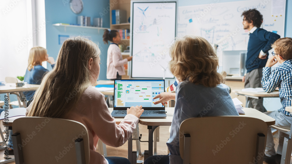 Wall mural elementary school science class: over the shoulder little boy and girl use laptop with screen showin