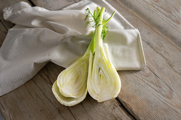 Fresh raw fennel bulb halved, healthy vegetable to cook a Mediterranean summer dish on a napkin and rustic wooden planks, copy space - obrazy, fototapety, plakaty