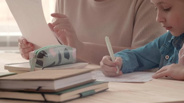 Close up of Caucasian teenage girl is doing home task together with her mom. Woman is checking her daughter math homework