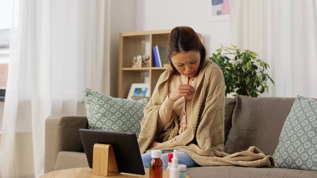 healthcare, technology and people concept - sick asian woman in blanket with thermometer having video call on tablet pc computer at home