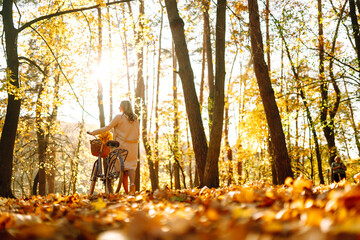 Stylish woman with a bicycle enjoying autumn weather in the park. Beautiful Woman walking  in the...