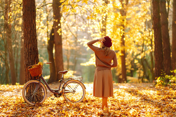Stylish woman with a bicycle enjoying autumn weather in the park. Beautiful Woman walking  in the autumn forest.