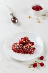 Raspberry ice cream from aquafaba with pistachios on a white plate.