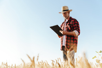 Image of pleased adult man looking aside while standing at cereal field