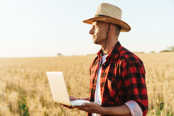 Image of adult man working with laptop while standing at cereal field