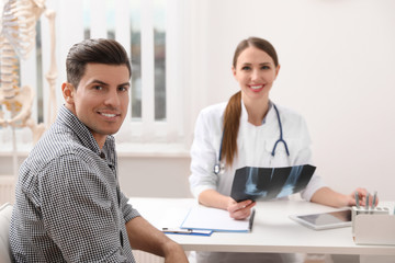 Orthopedist showing X-ray picture to patient at table in clinic