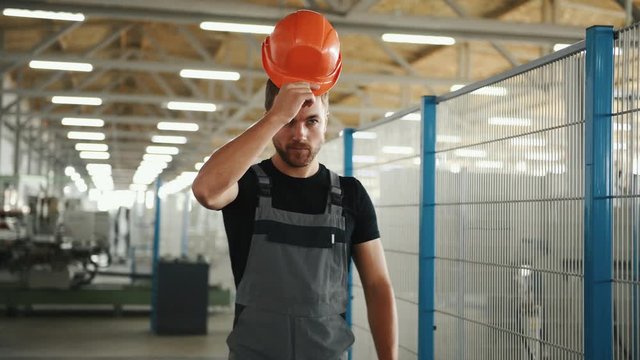 Employee in grey uniform and with orange hard hat walks in the factory.