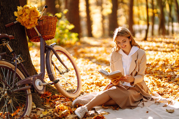 Stylish woman reading a book in the autumn park. Relaxation, enjoying, solitude with nature. - obrazy, fototapety, plakaty