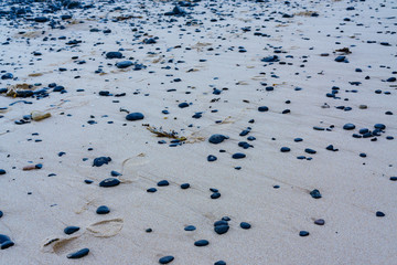 Small black pebbles on smooth light pale brown beach sand