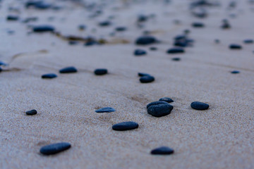 Fototapeta na wymiar Black pebbles on light brown sand