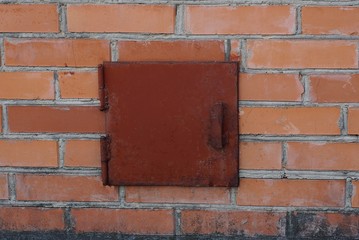 iron rusty red lid on a small square entrance on a brown brick wall
