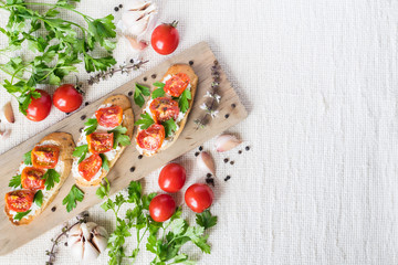 Italian bruschetta with tomatoes and greens on wooden cuting board, overview, copyspace