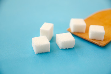 Sugar cubes lie on a wooden spoon and a blue background, copy space