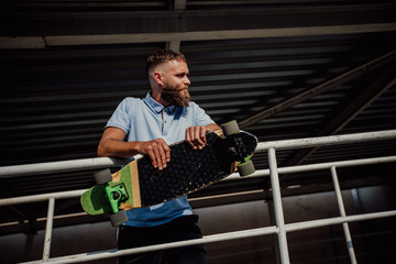 Handsome young stylish hipster guy with beard with a longboard