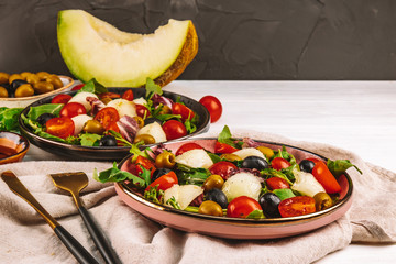  Italian cuisine - two servings of salad with melon, tomatoes and olives on a white wooden plate. Free space for the text.