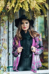 Beautiful model posing for photos in a room. Wearing black pants, hat and purple blouse. 