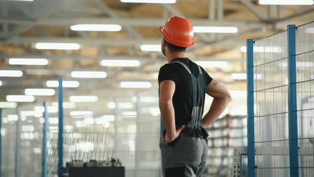 Technician in grey uniform looks around in the factory and takes off his protective helmet.