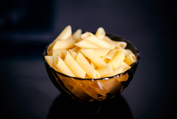 Cooked gluten free pasta penne in glass bowl. Black background.