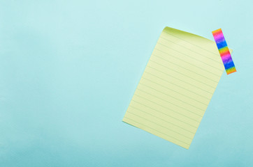 Top view of lined yellow sheet of paper and colorful tape on the blue blank surface
