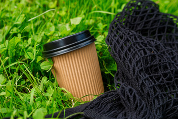 Hot paper Craft cup of coffee with black bag on the grass on a morning. Take away or delivery concept. Copy space. Summer lifestyle. Place for your text or logo on mug, mockup