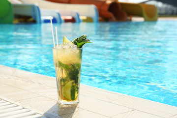 Glass of delicious mojito near swimming pool, space for text. Refreshing drink