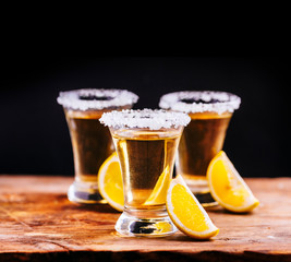 Tree shot glasses of Mexican tequila cocktail with lemon slices and salt on wooden table with black background