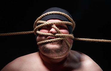 Portrait of binded fat man in cap with rope on face
