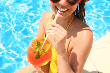 Woman with glass of refreshing drink near swimming pool, closeup