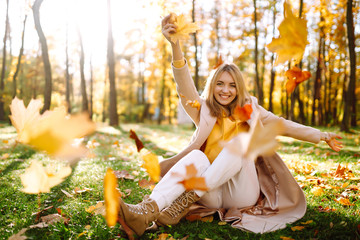 Smiling woman playing with autumn  yellow leaves.  Stylish woman enjoying autumn weather in the...