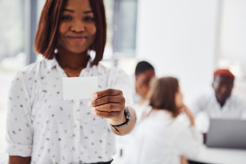 Woman holds business card card. Group of african american people working in office together