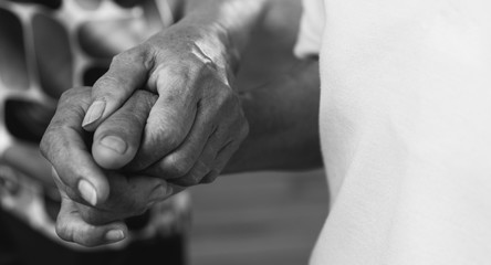 Caregiver, carer hand holding elder hand in hospice care background. Philanthropy kindness to disabled old people concept in black and white 