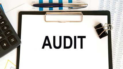 The word AUDIT written on a white sheet of paper on the background of graphs next to pencils