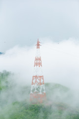 High voltage transmission towers on mountain with fog.
