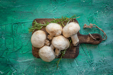 Angri, Italy. Small group of raw white champignon mushrooms with rosemary sprigs on wooden cutting board on green backdrop.