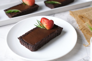 Rectangular chocolate tart with strawberry in white plate set in cafe table.