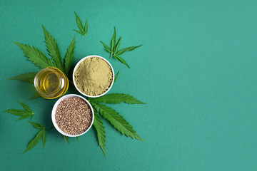 Hemp products - cannabis leaves, seeds, hemp oil and protein powder, flour on green background. Top...