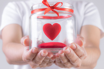 The woman is holding a jar with red heart inside. Concept for charity, health insurance, love,...