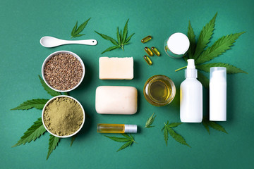 Fototapeta na wymiar Flat lay with hemp extract products - cosmetics, lotion, face cream, body butter, soap bars, cannabis leaves, seeds, hemp oi, capsules, protein powder, flour on green background. Top view. Copy space